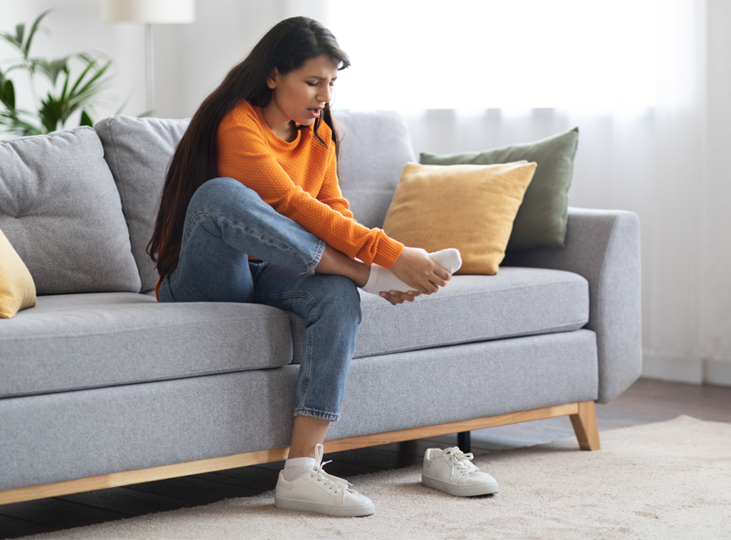 woman sitting on a couch holding her foot in pain