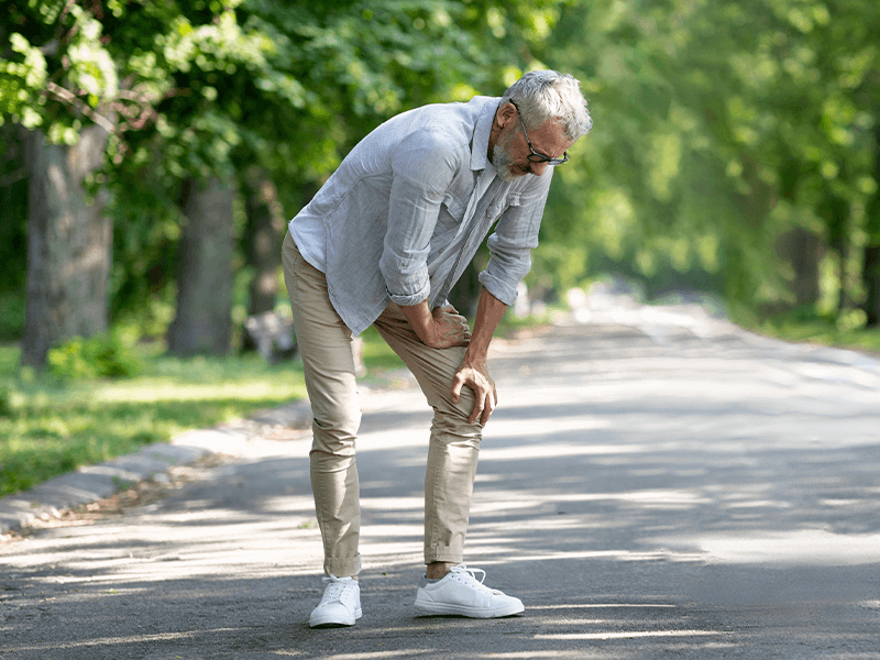 older man experiencing knee pain while walking outdoors