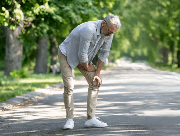 older man experiencing knee pain while walking outdoors 